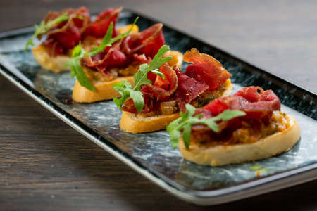 bruschetta with spicy chopped beef and fries on white bread. decorated with parsley leaves. sandwiches on a blue marble plateの写真素材