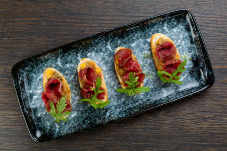 bruschetta with spicy chopped beef and fries on white bread. decorated with parsley leaves. sandwiches on a blue marble plate. view from aboveの写真素材