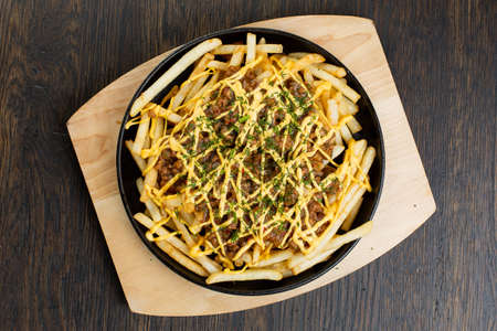 French fries with chopped beef in a metal frying pan on a wooden board. fried meat rolls with cheese sauce. view from above. fast foodの写真素材