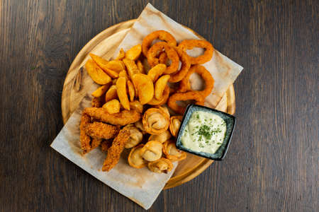 assorted fries of onion rings, French fries, chicken nuggets and fried dumplings with creamy sauceの写真素材