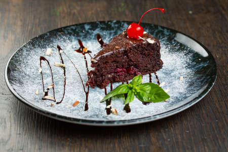 chocolate dessert with cherry filling and nuts. a slice of cake decorated with liquid chocolate and a mint leafの写真素材
