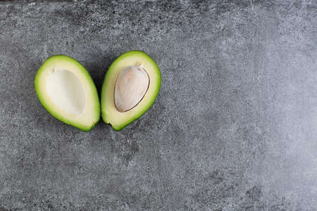 two green avocados lie on an artificial stone board. diet food. green vegetable. avocado cutaway. avocado seed. space for design and for textの写真素材
