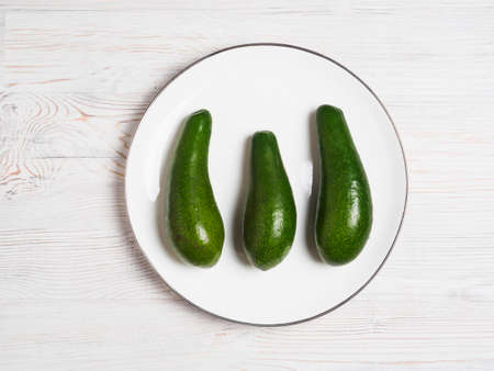 3 avocados on white plate on wooden surfaceの写真素材