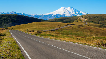 Wavy road through the autumn hills to the distant snowy mountainの写真素材
