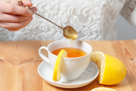 cup of tea with a lemon on a wooden table to which a spoon add honeyの写真素材