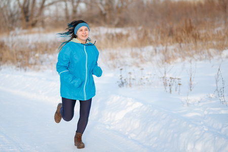 Running sports woman in a blue jacket. Jogging in the winter outdoors in the snowの写真素材