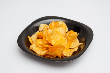 handful of potato chips on black plate on white cloth background