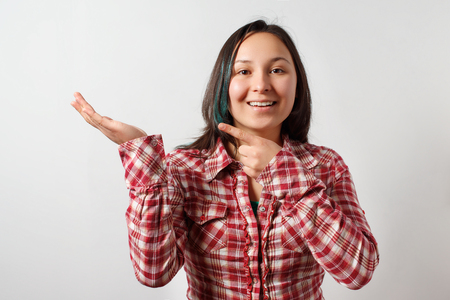 a young girl shows her finger on the palm of the other hand, looks into the frame and smiles. On light grey backgroundの写真素材
