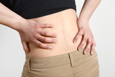 Long working hours and health. Young female with backache. Woman with back pain on gray backgroundの写真素材
