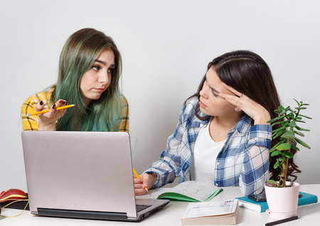 Two young student girls with laptops studying together at the table.の写真素材
