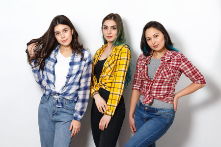 portrait of three young beautiful slender girls women in plaid shirts red, yellow and blue. on white...