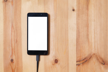 Close up smartphone, and data connecting cable for transfer and Charge battery on the wood floor background and texture use for technology concept.の写真素材