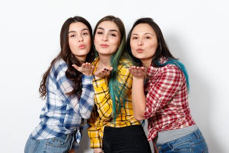 three attractive young woman with shiny makeup sending air kiss, looking at camera, on white background.の写真素材