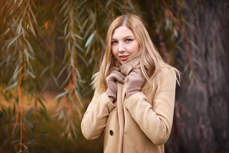 portrait of a young beautiful woman blonde girl in a beige coat on the background of an autumn Parkの写真素材