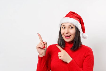 portrait of a sweet dreamy young woman in a red sweater and Christmas hat. on white background. place for copy space.の写真素材