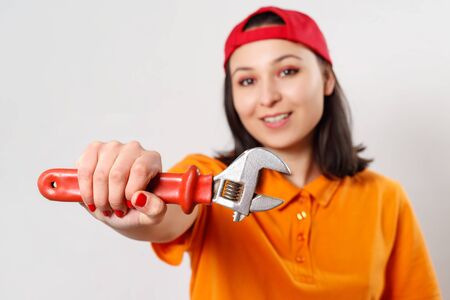 portrait of a young woman with a wrench in her hand. on white background. face infocus, focusing on a wrenchの写真素材