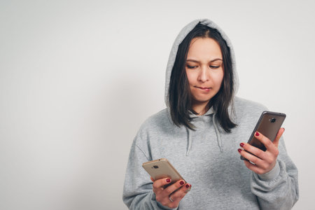 portrait of a young woman in a hoodie with two smartphones on a white background