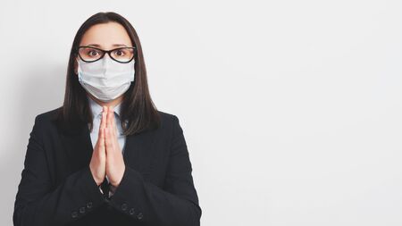 female in medical mask praying with and clasped hands for coronavirus epidemic end against gray background with copy spaceの写真素材
