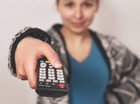 Girl holding a TV remote, changing the channel. Woman sitting at home with the remote control watching television alone.の写真素材