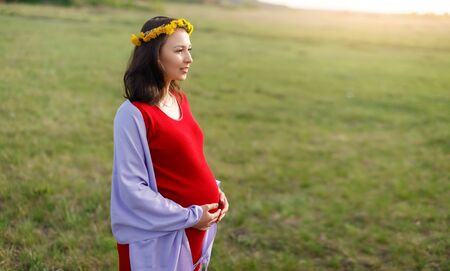 happy young pregnant woman walking in the fresh air in the afternoon in a red dress. Concept of pregnancy, waiting for a child.の写真素材