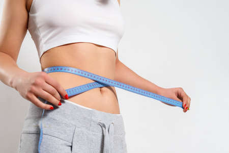 A young woman measures her waist with a measuring tape. On a white background.の写真素材