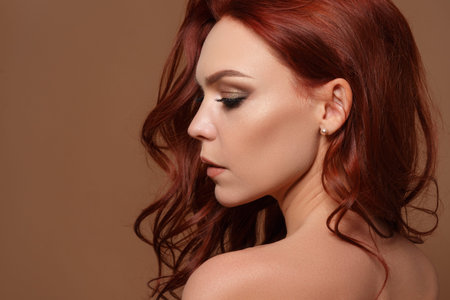 Beauty portrait of a red-haired beautiful woman on a beige background. With a copy space.