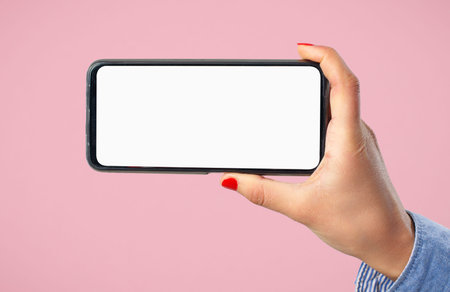 A woman's hand holds a smartphone with a blank white screen horizontally. Against a pink background.