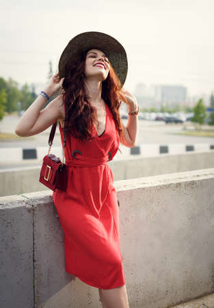 A happy young woman, holding a wide hat, poses in city park in summerの写真素材