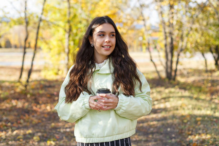 Portrait of a joyful young woman with a cup of coffee in an autumn parkの写真素材