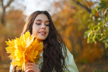 A happy young woman in an autumn park with a bunch of maple leaves in her handsの写真素材