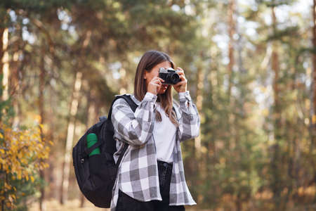 A young female tourist walks in the forest with a camera and a backpack on her shouldersの写真素材