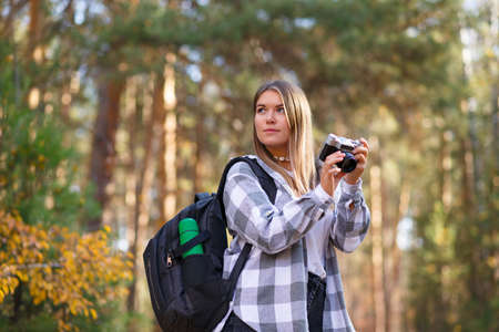 A young female tourist walks in the forest with a camera and a backpack on her shouldersの写真素材