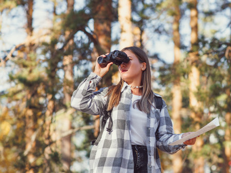 A young tourist walks through the autumn forest with a backpack, looking into the distance through...