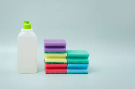Sponges for washing dishes of different colors and a bottle of liquid detergent on a blue background.の写真素材