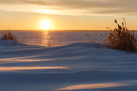 Frozen lake coast at colorful sunset. Shooting from the bottom position. Sunlight reflects off ice and snow crust.の写真素材