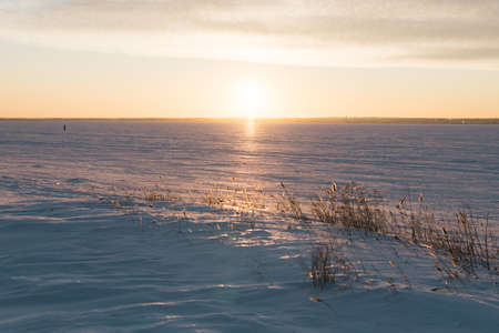 Frozen lake coast at colorful sunset. Shooting from the bottom position. Sunlight reflects off ice and snow crust.の写真素材