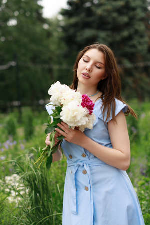 Portrait of a beautiful young woman in a blue dress with a bouquet of peonies.の写真素材
