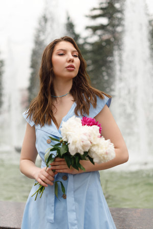 Portrait of a beautiful young woman in a blue dress with a bouquet of peonies.