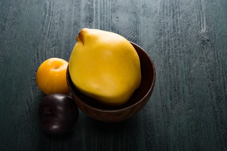 yellow quince and plums in brown wooden bowl on the dark tableの写真素材