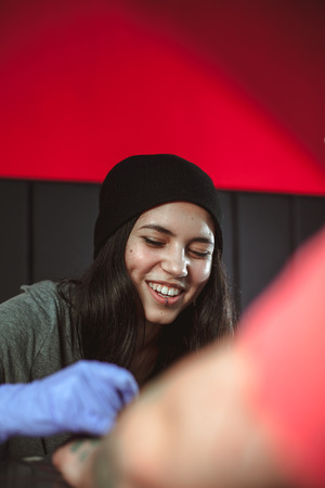 Beautiful brunette girl makes tattoo. Tattooist makes a tattoo. Closeupの写真素材