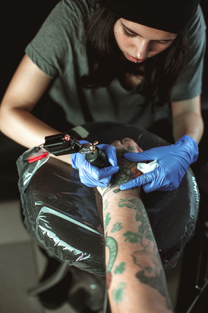 Beautiful brunette girl makes tattoo. Tattooist makes a tattoo. Closeupの写真素材