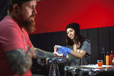 Beautiful brunette girl makes tattoo. Tattooist makes a tattoo. Closeupの写真素材