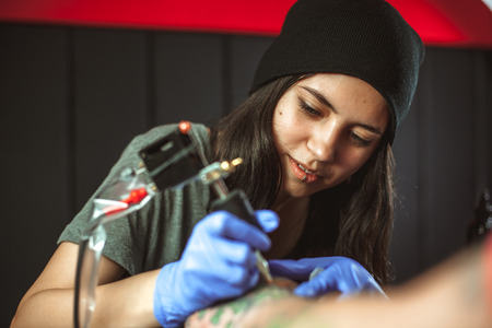Beautiful brunette girl makes tattoo. Tattooist makes a tattoo. Closeupの写真素材