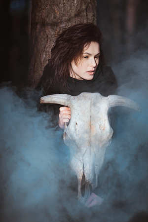 Young witch with skull in night forestの写真素材