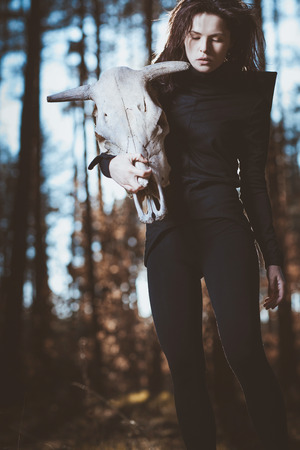 Young witch with skull in night forestの写真素材