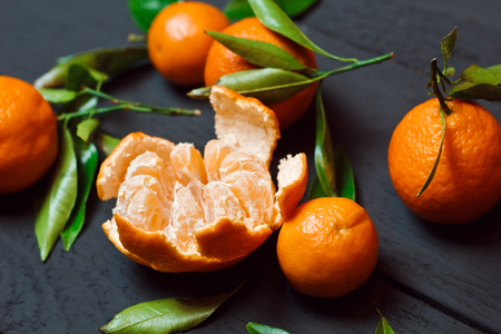 Beautiful ripe tangerines with leaves on a black wooden backgroundの写真素材