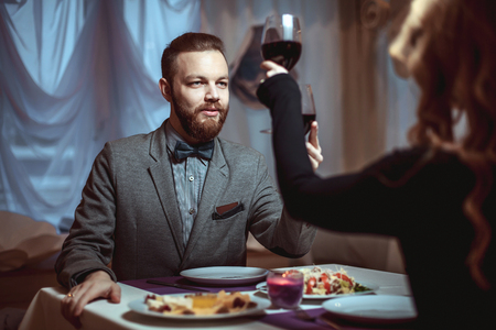 Beautiful young couple with glasses of red wine in luxury restaurantの写真素材