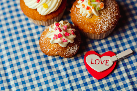 Beautiful cupcakes and a heart with the inscription Love lie on a vintage checkered tableclothの写真素材