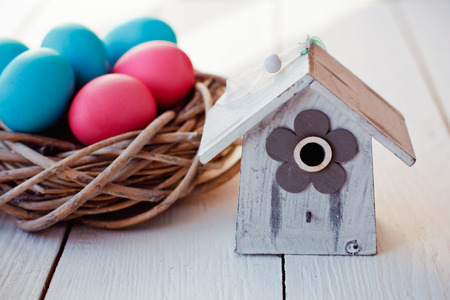 color Easter eggs in nest on white wooden background with birdhouseの写真素材