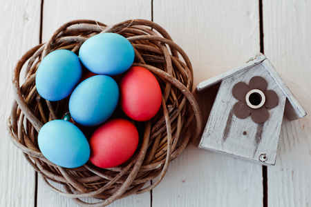 color Easter eggs in nest on white wooden background with birdhouseの写真素材